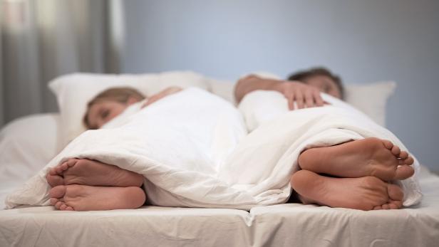 Ein Paar schläft Rücken an Rücken in einem Bett unter einer weißen Decke.