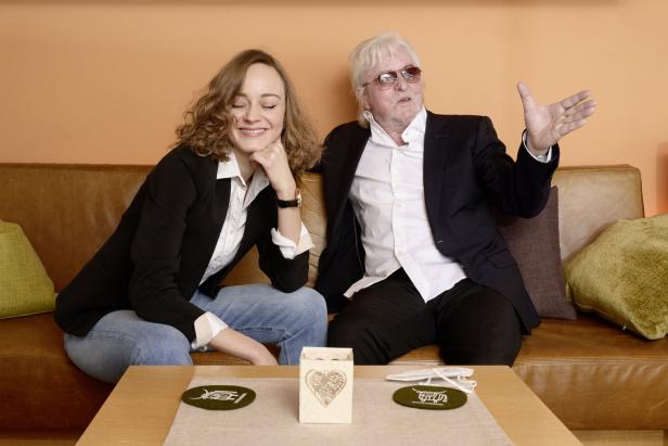 Eine junge Frau und ein älterer Mann sitzen auf einem Sofa und unterhalten sich.