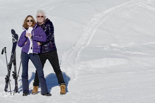 Ein Paar in Winterkleidung steht im Schnee, Skier lehnen daneben.