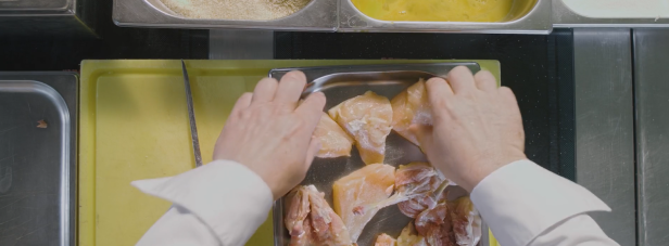 Ein Koch bereitet Hähnchenfleisch in einer Küche zu.