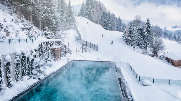 Ein beheizter Außenpool mit Blick auf eine schneebedeckte Skipiste in einem Winterresort.