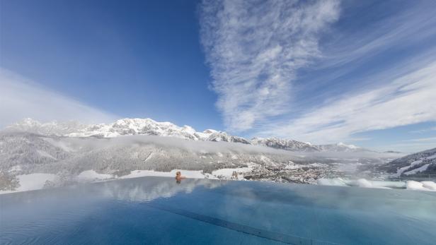 Eine Frau entspannt in einem Infinity-Pool mit Blick auf schneebedeckte Berge.