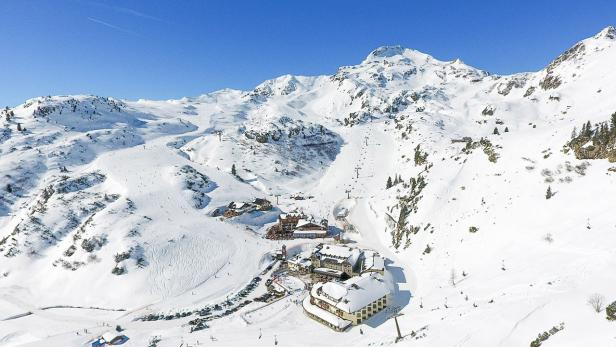 Ein verschneites Skigebiet mit Liften und mehreren Gebäuden unter blauem Himmel.