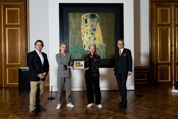 Vier Personen stehen vor Gustav Klimts Gemälde „Der Kuss“ und halten ein Tablet.