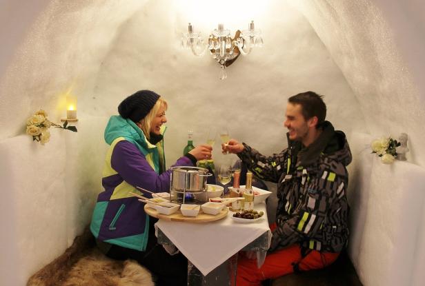 Ein Paar stößt in einem Iglu-Restaurant mit Champagnergläsern an.