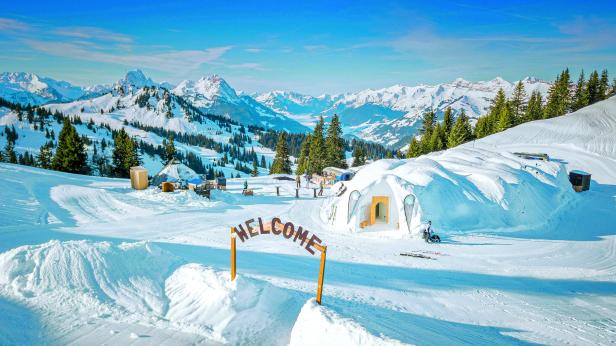 Ein Iglu-Dorf mit „Welcome“-Schild im verschneiten Berggebiet.