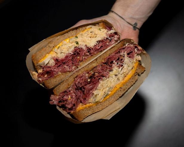 Ein aufgeschnittenes Reuben-Sandwich mit Corned Beef, Sauerkraut und Käse wird von einer Hand gehalten.