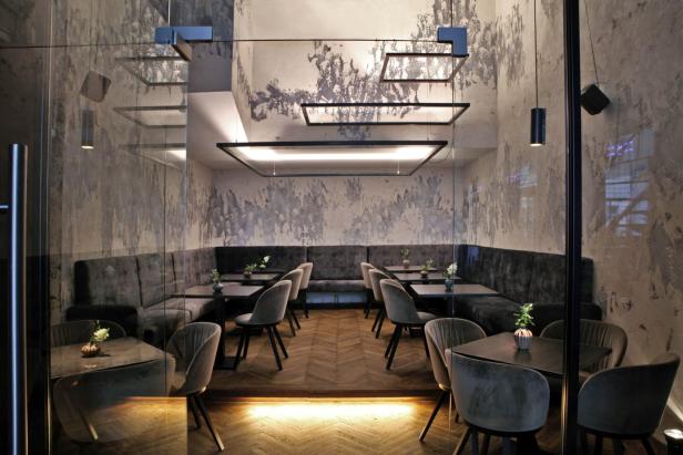 Ein elegantes Restaurant mit grauen Samtstühlen und dunklen Holztischen.