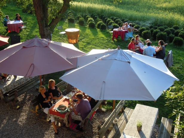 Ein Gartenrestaurant mit Gästen an Tischen unter Sonnenschirmen.