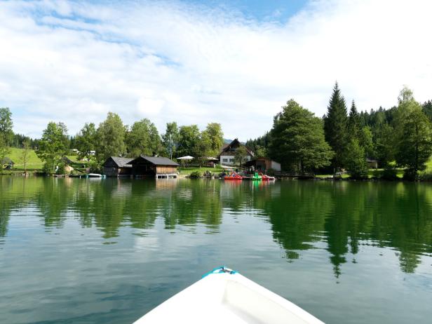 Blick von einem Boot auf einen ruhigen See mit Häusern und Bäumen am Ufer.