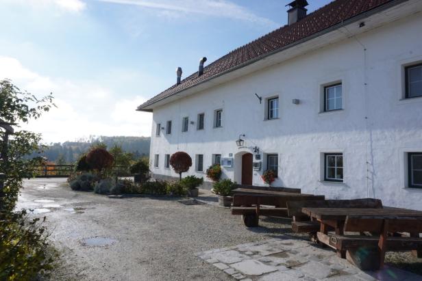 Ein weißes Gebäude mit braunem Dach und Holzbänken im Außenbereich.