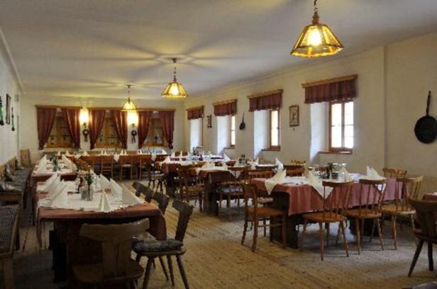 Ein Speisesaal mit gedeckten Tischen und hölzernen Stühlen unter warmem Licht.