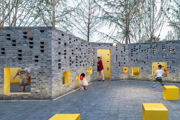 Kinder spielen in einem architektonisch gestalteten Bereich mit Mauern und gelben Akzenten.