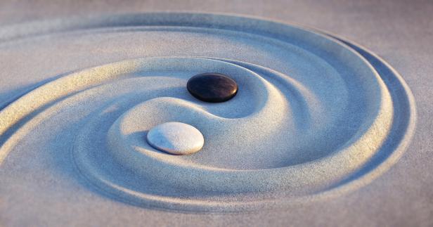 Ein Zen-Garten mit einem Yin-und-Yang-Symbol aus geharktem Sand und zwei Steinen.