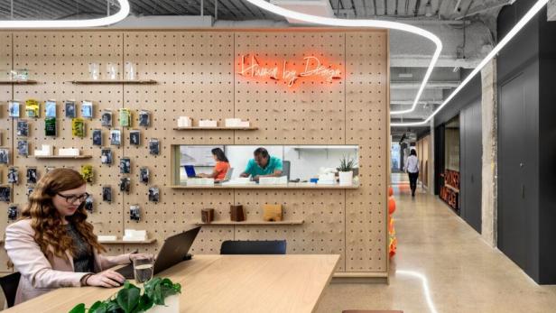 Eine Frau arbeitet an einem Laptop in einem modernen Büro mit dem Schriftzug „Human by Design“.