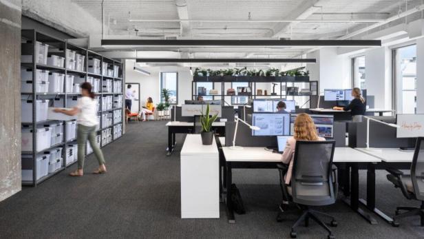 In einem modernen Büro arbeiten Menschen an Computern und ordnen Gegenstände in Regalen ein.