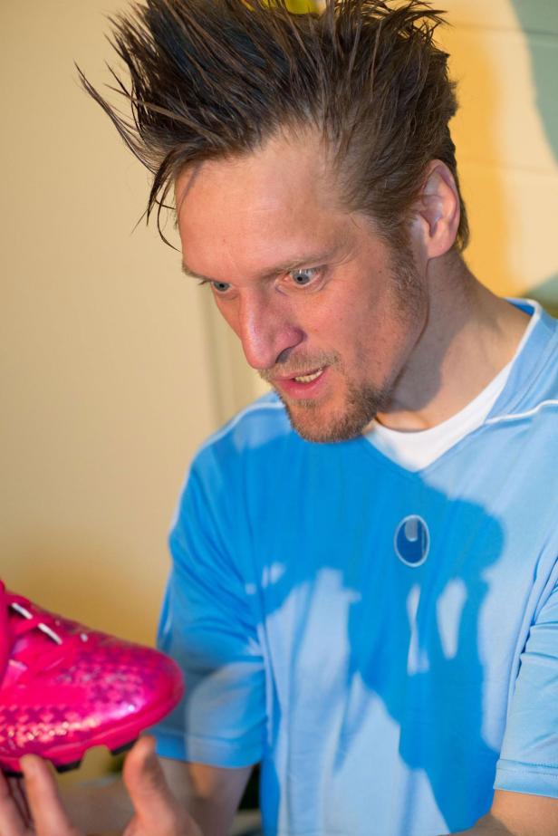 Ein Mann im Sporttrikot betrachtet einen pinkfarbenen Fußballschuh.