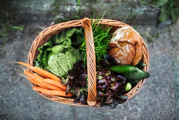 Ein Korb gefüllt mit Gemüse und Brot, darunter Karotten, Salat, Gurken und ein Brotlaib.