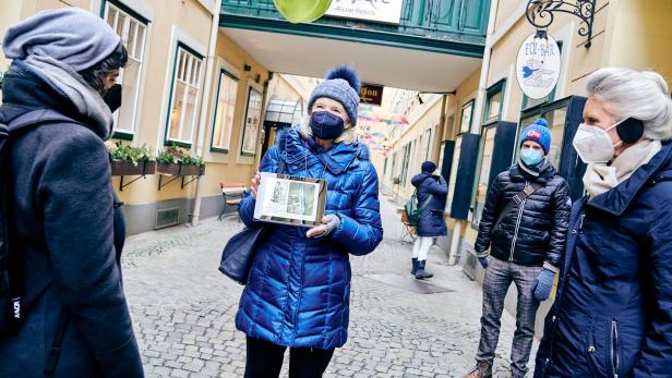 Eine Frau zeigt auf einem Tablet historische Bilder in einer Gasse in Wien.