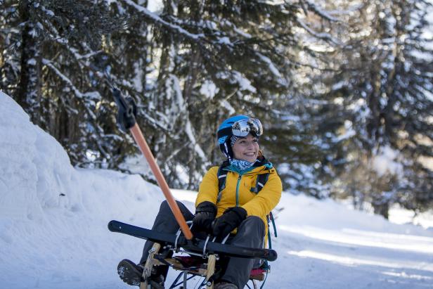 Eine Frau sitzt auf einem Schlitten im Schnee und lächelt.