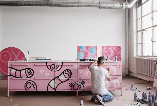 Ein Mann bemalt ein rosa Sideboard mit Graffiti in einem Atelier.