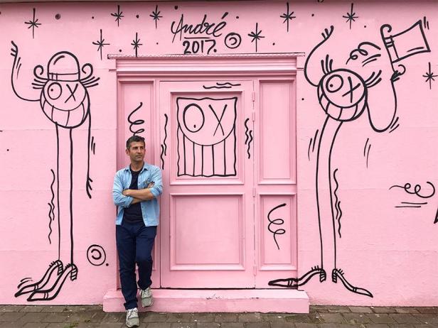 Ein Mann steht vor einer rosa Wand mit Graffiti des Streetart-Künstlers André.