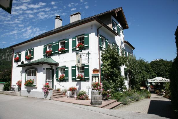 Das Gasthaus „Wirt am Gries“ mit grünen Fensterläden und Blumenkästen an einem sonnigen Tag.