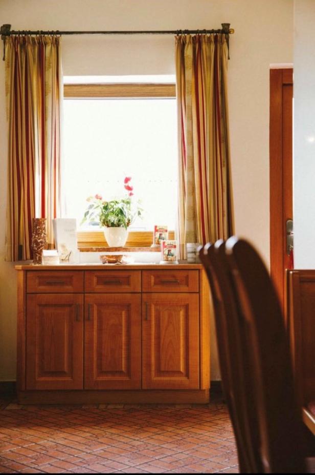 Ein Holzschrank steht vor einem Fenster mit rot gestreiften Vorhängen.