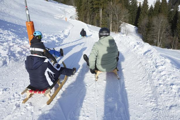 Mehrere Personen rodeln auf einer schneebedeckten Rodelbahn bergab.