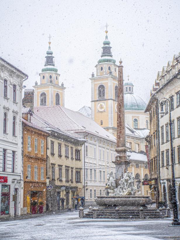 Schneefall in Ljubljana mit Blick auf die Türme der Franziskanerkirche und den Herkulesbrunnen.