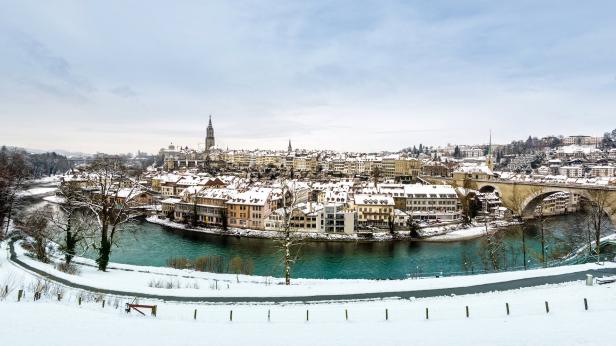 Winterliche Ansicht der Stadt Bern mit schneebedeckten Dächern und der Aare.