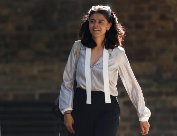 Eine Frau mit dunklen Haaren und einer hellen Bluse lächelt.