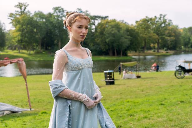 Eine Frau in einem hellblauen Kleid steht auf einer Wiese vor einem See.