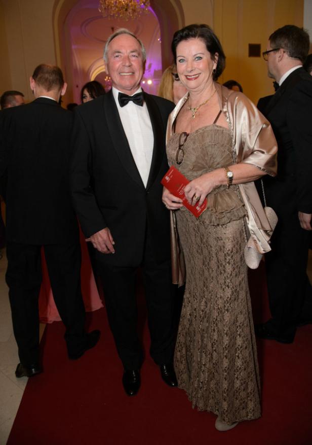 Ein Mann im Smoking und eine Frau im Abendkleid posieren auf einem roten Teppich.