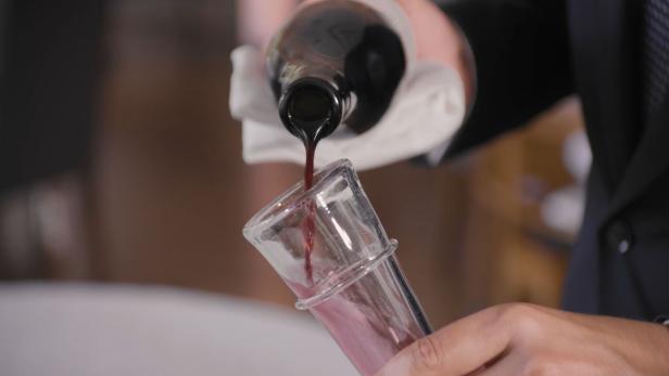 Eine Person gießt eine dunkle Flüssigkeit aus einer Flasche in ein Glas.