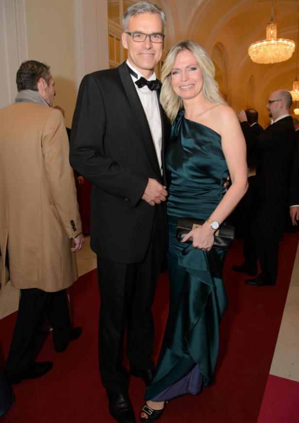 Ein Mann im Smoking und eine Frau im Abendkleid posieren auf einem roten Teppich.