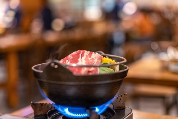 Ein Topf mit Sukiyaki köchelt auf einem Gaskocher.