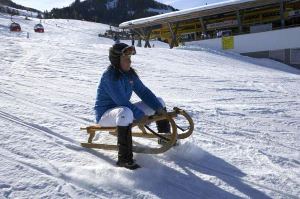 Eine Frau fährt mit einem Holzschlitten einen schneebedeckten Hang hinunter.