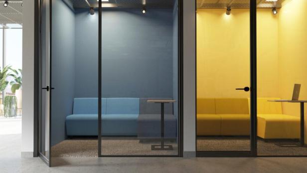 Zwei Telefonzellen mit Glaswänden, eine blau und eine gelb, mit Sofas und Tischen.