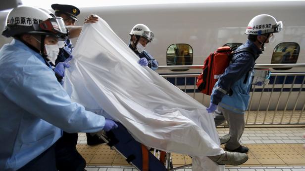 Rettungskräfte transportieren eine Person, die mit einem weißen Tuch bedeckt ist, von einem Shinkansen-Zug.