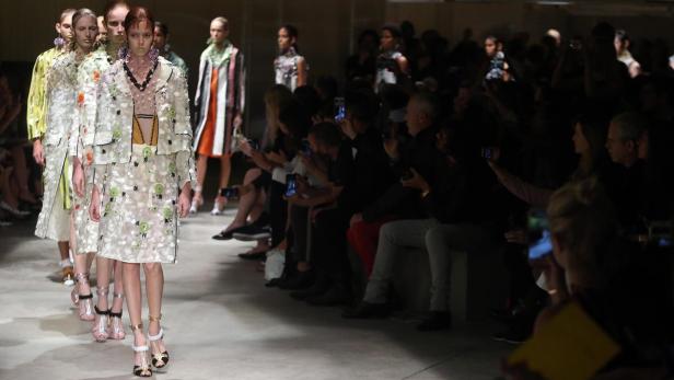 Models präsentieren florale Ensembles auf einem Laufsteg vor einem Publikum.