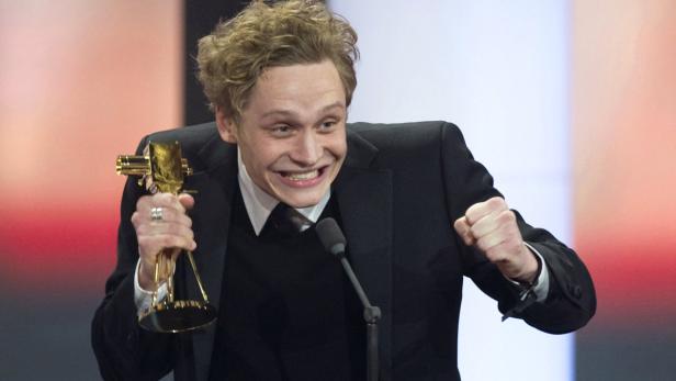Ein Mann im Anzug freut sich mit einer goldenen Auszeichnung in der Hand.