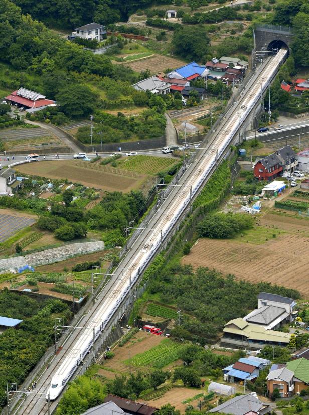 Ein Shinkansen-Hochgeschwindigkeitszug fährt durch eine ländliche japanische Landschaft.