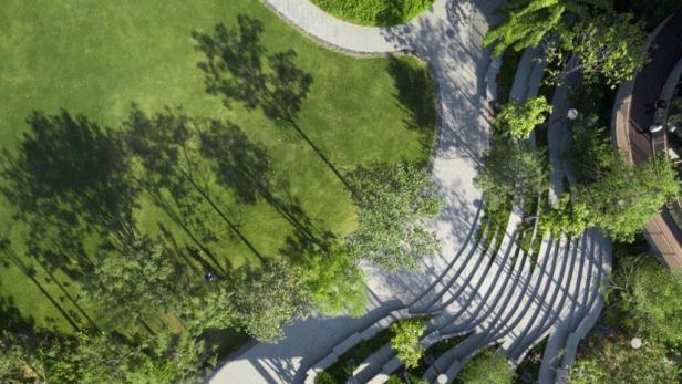 Luftaufnahme eines Parks mit Rasenflächen, Bäumen und geschwungenen Wegen.