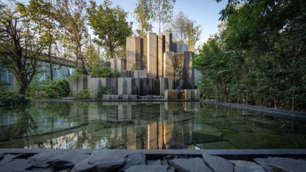 Ein künstlicher Wasserfall aus Betonblöcken in einem Garten wird im Wasser reflektiert.