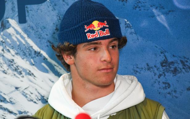 Ein junger Mann mit einer Red Bull Mütze vor einem Hintergrund mit Bergmotiv.