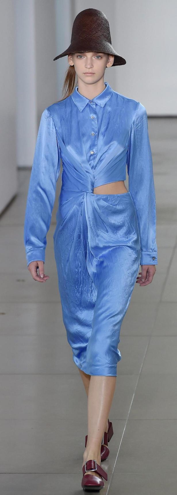 Eine Frau mit Hut trägt ein blaues Kleid mit Cut-Out an der Taille.