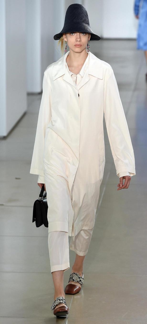 Eine Frau mit Hut und hellem Mantel auf einem Laufsteg.