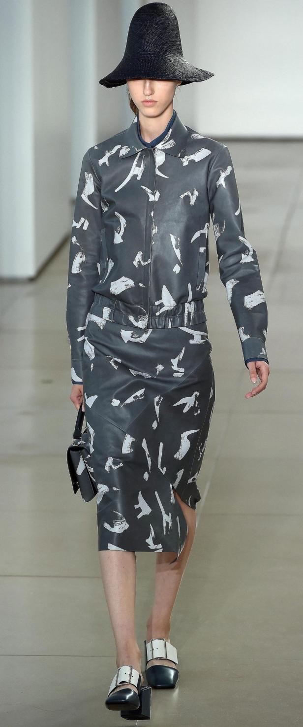 Eine Frau in einem grauen Anzug mit weißem Muster und einem schwarzen Hut.