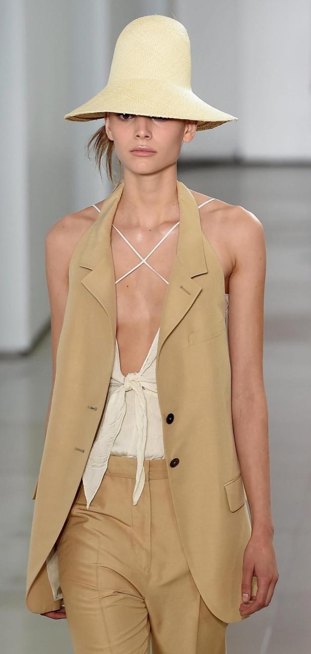 Eine Frau trägt einen Strohhut, eine beige Weste und eine helle Hose.